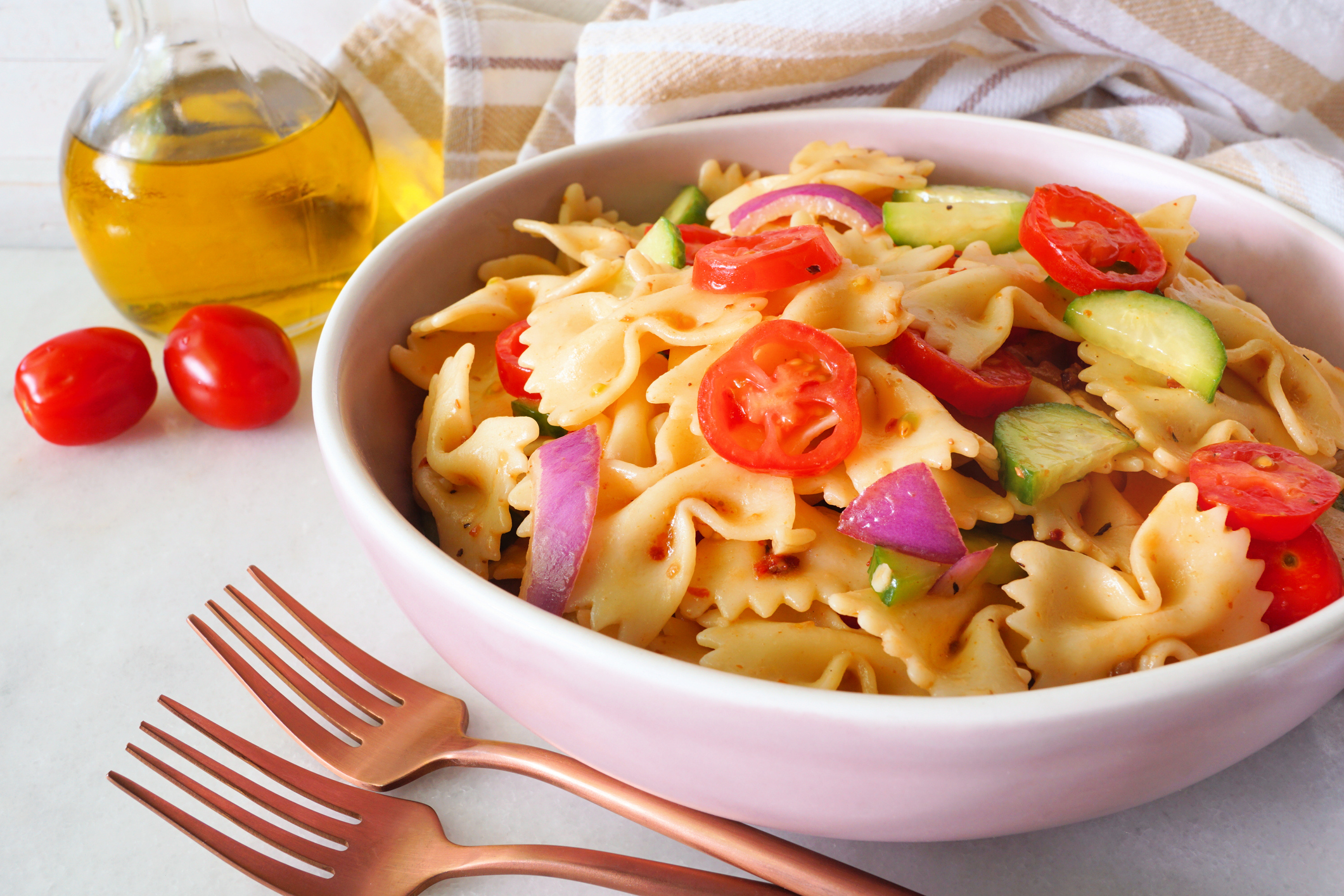 Traditional pasta salad with tomatoes, onion and cucumbers. Close up table scene with a white marble background.