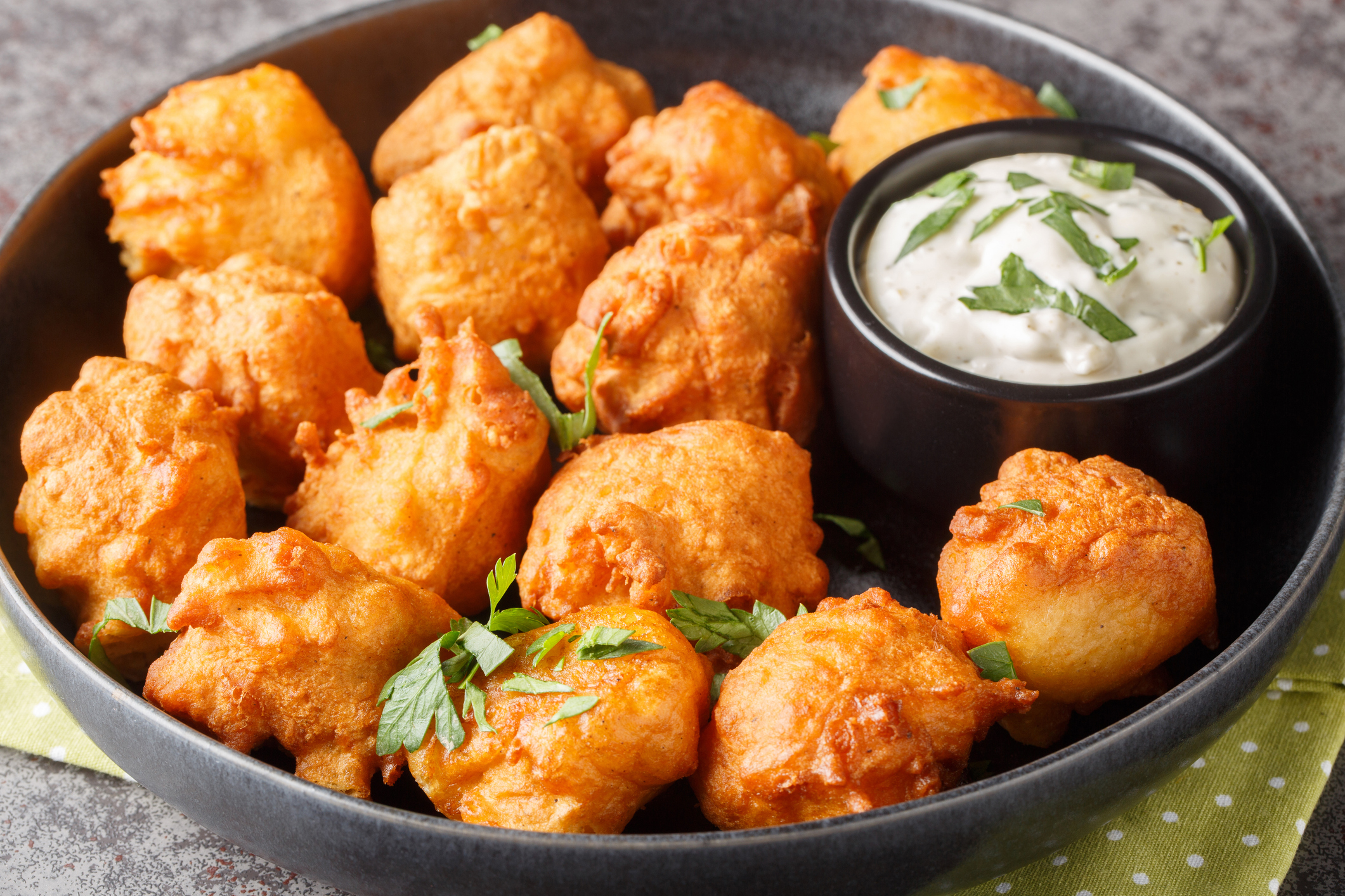 Hush puppies is made with eggs, onion, self-rising flour, and cornmeal, then deep-fried until crisp and golden closeup on the plate on the table. Horizontal