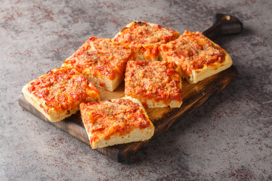 Sfincione typical oven-baked focaccia very soft and seasoned with tomato, onion, anchovies, cheese, oregano and bread crumbs closeup on the wooden board on the table. Horizontal