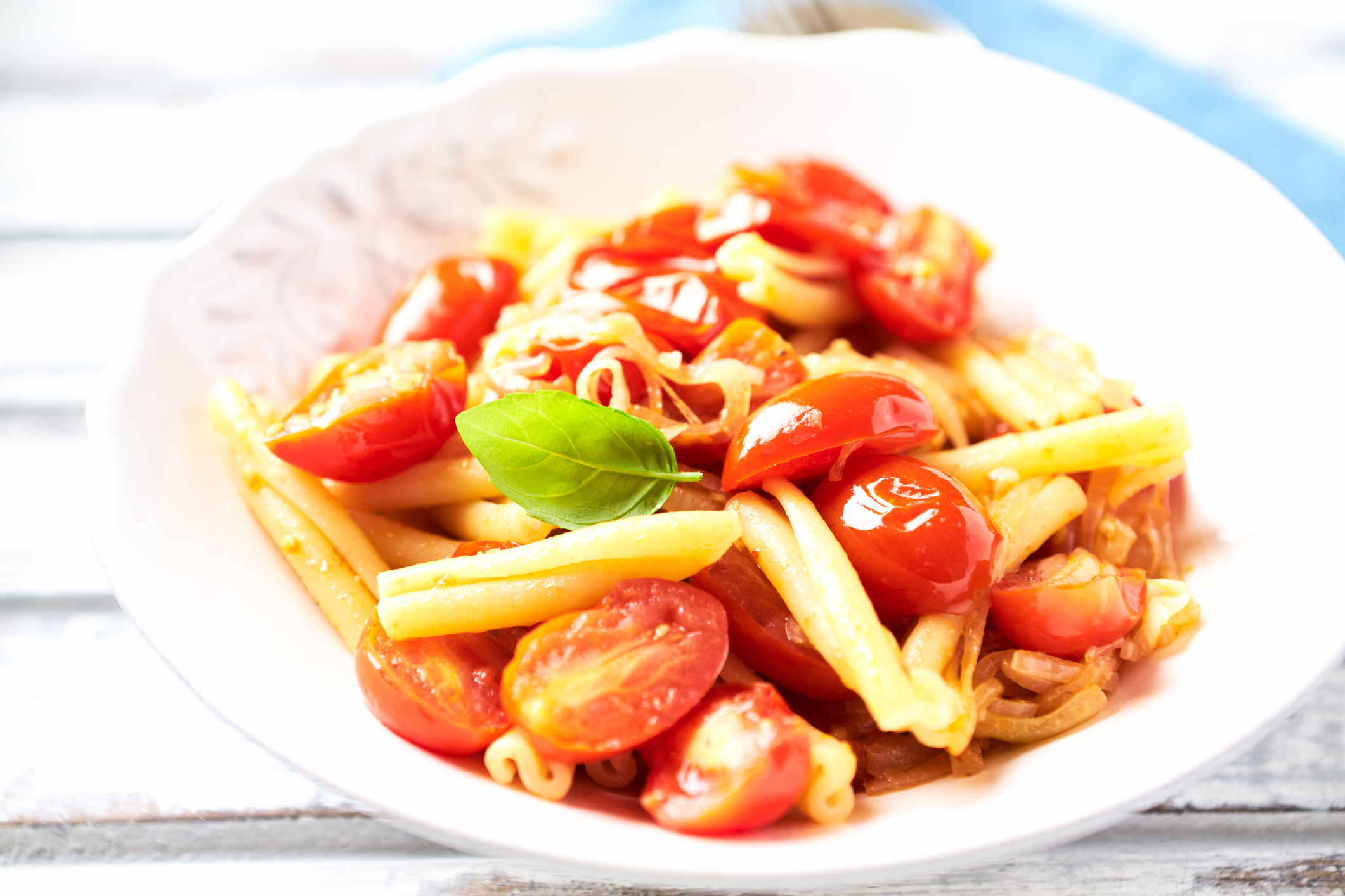 Casarecce pasta withe cherry tomatoes and fresh basil. Bright wooden background.