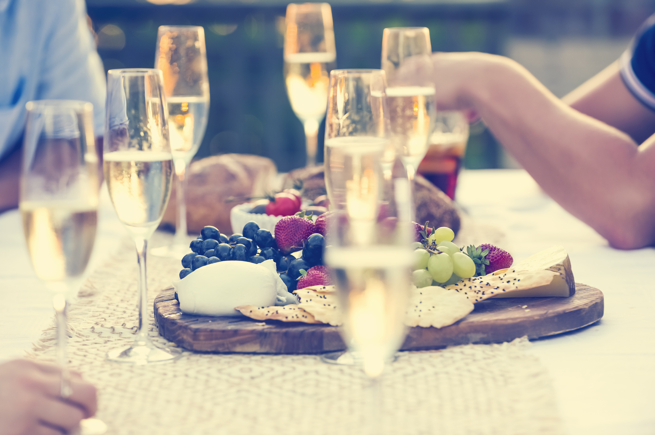 Group of friends drinking champagne. They are having a dinner party at sunset with a cheese and fruit platter. They are outdoors