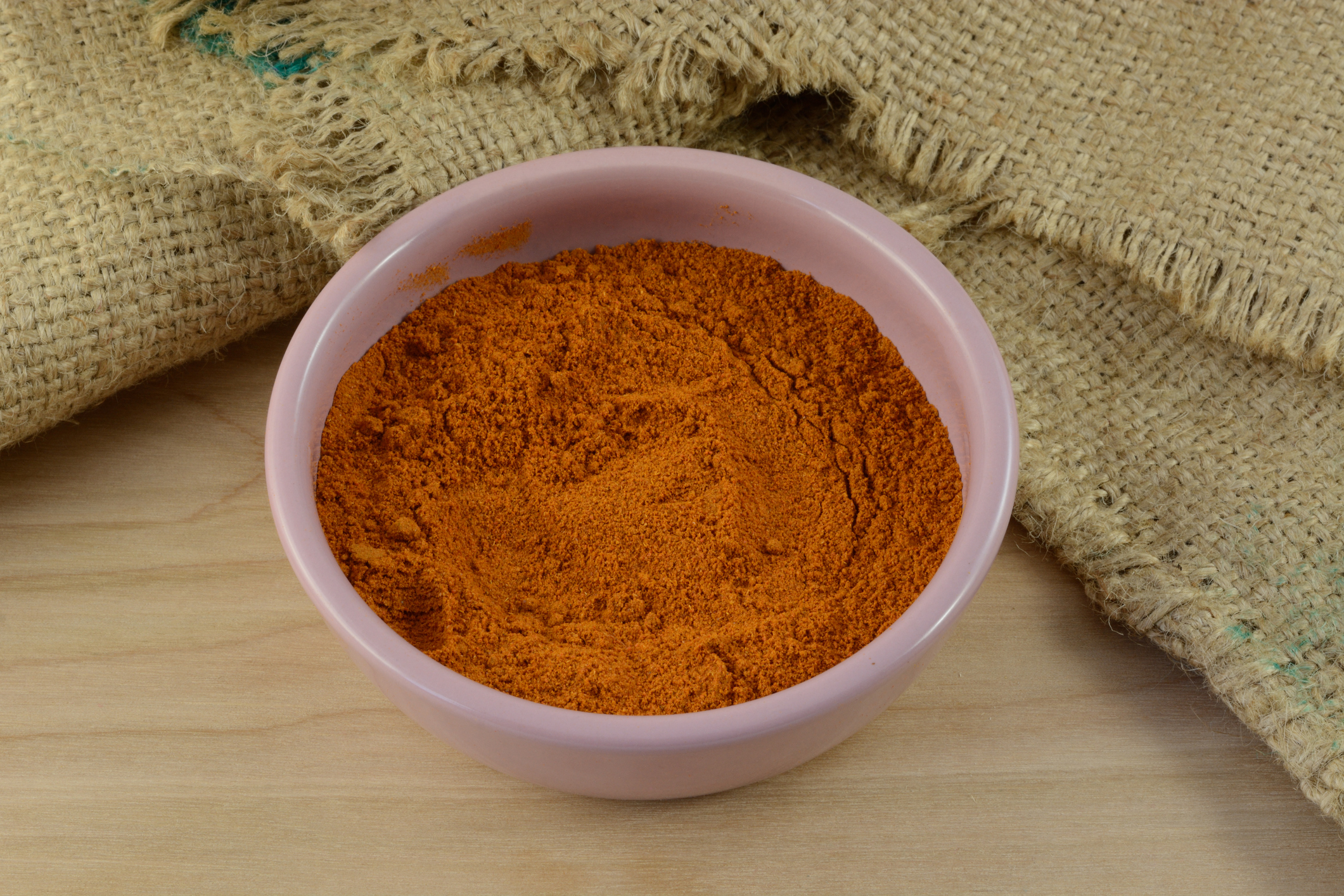 Ground red pepper spice in pink condiment bowl on wooden table with burlap