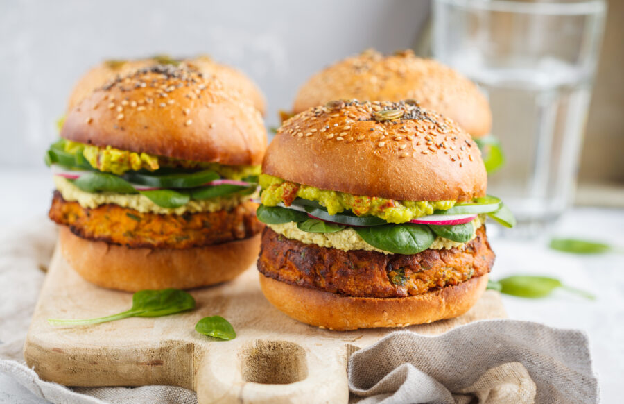 baked sweet potato burger with whole grain bun, guacamole, vegan mayonnaise and vegetables on a board. 