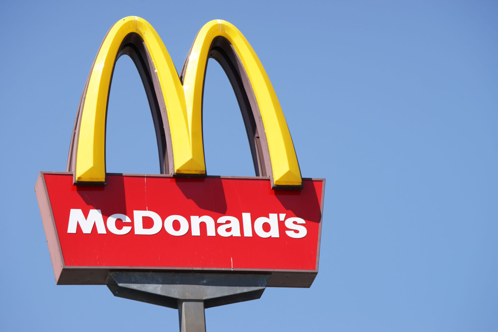 Close-up of McDonalds outdoor sign with typical rounded yellow M letter against cloudless blue sky. Sign is positioned on the left side of image.