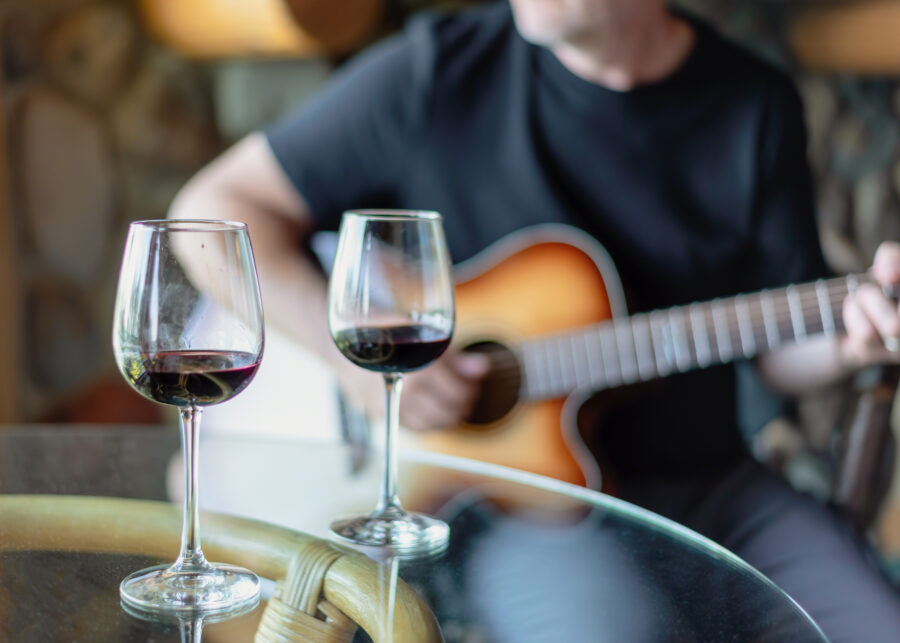 Man playing acoustic guitar with wine glasses in foreground