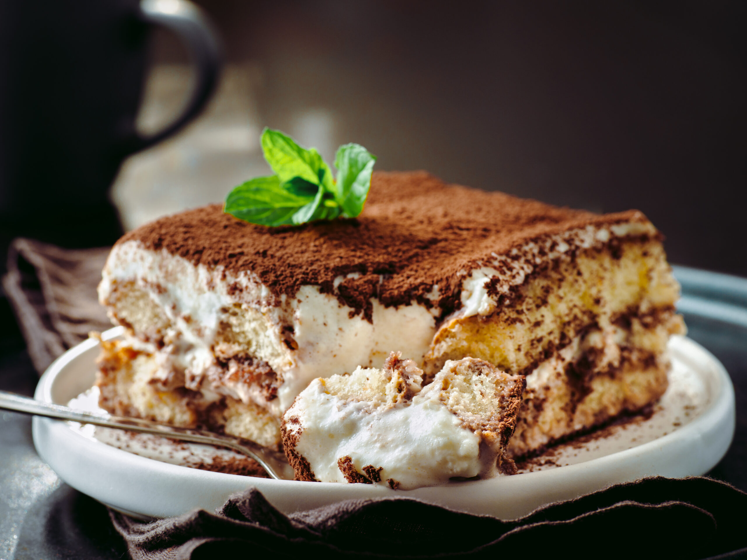 Perfect homemade tiramisu cake in spoon. Tiramisu portion on plate over dark tabletop background. Delicious no bake tiramisu ready-to-eat. Close up