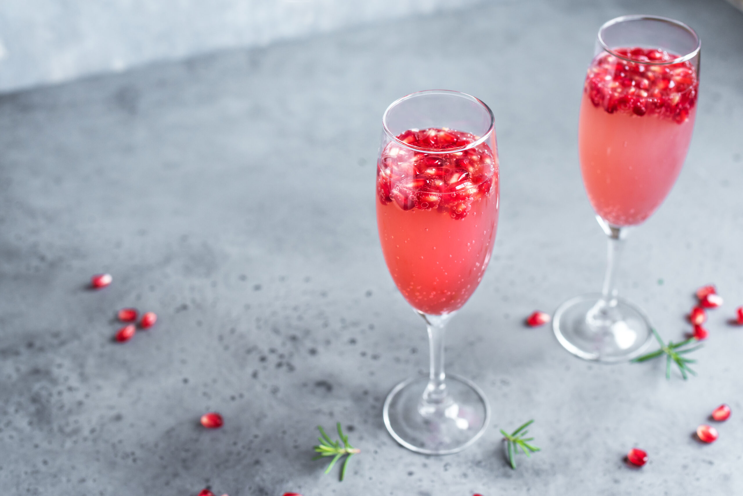 Pomegranate Champagne Mimosa Cocktail (Mocktail) with rosemary on concrete background, copy space. Mimosa Drink for Valentine Day or other holidays.