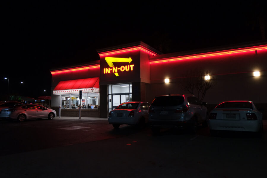 View at the In-n-out Burger restaurant  from the parking lot, at night. Patrons sitting and dinning inside. 