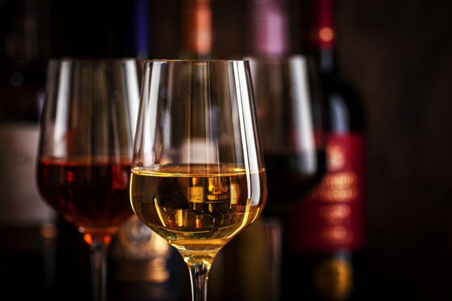 Red, white and rose wine in glasses on wooden background and collection of wine bottles