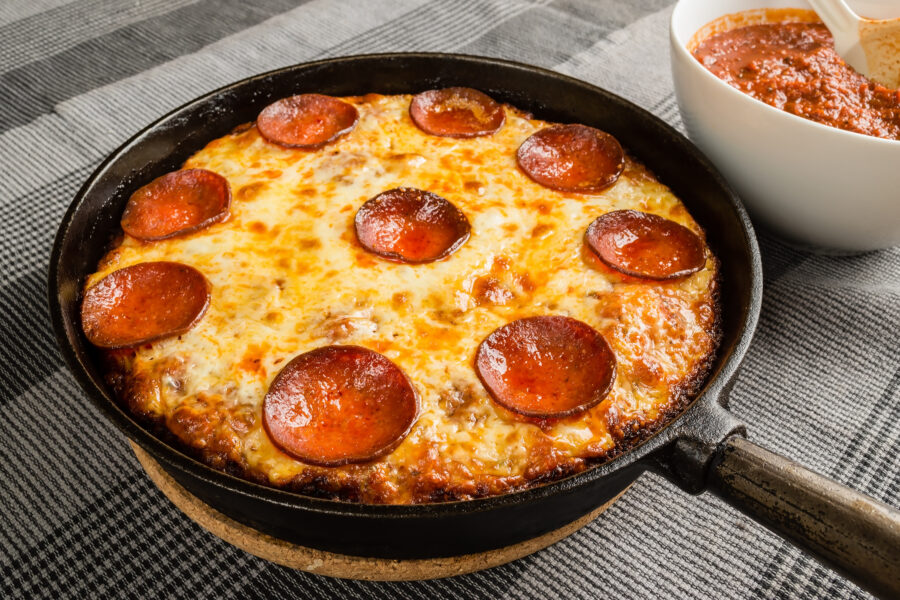 pan pizza with pepperoni salami and mozzarella in cast iron frying pan.