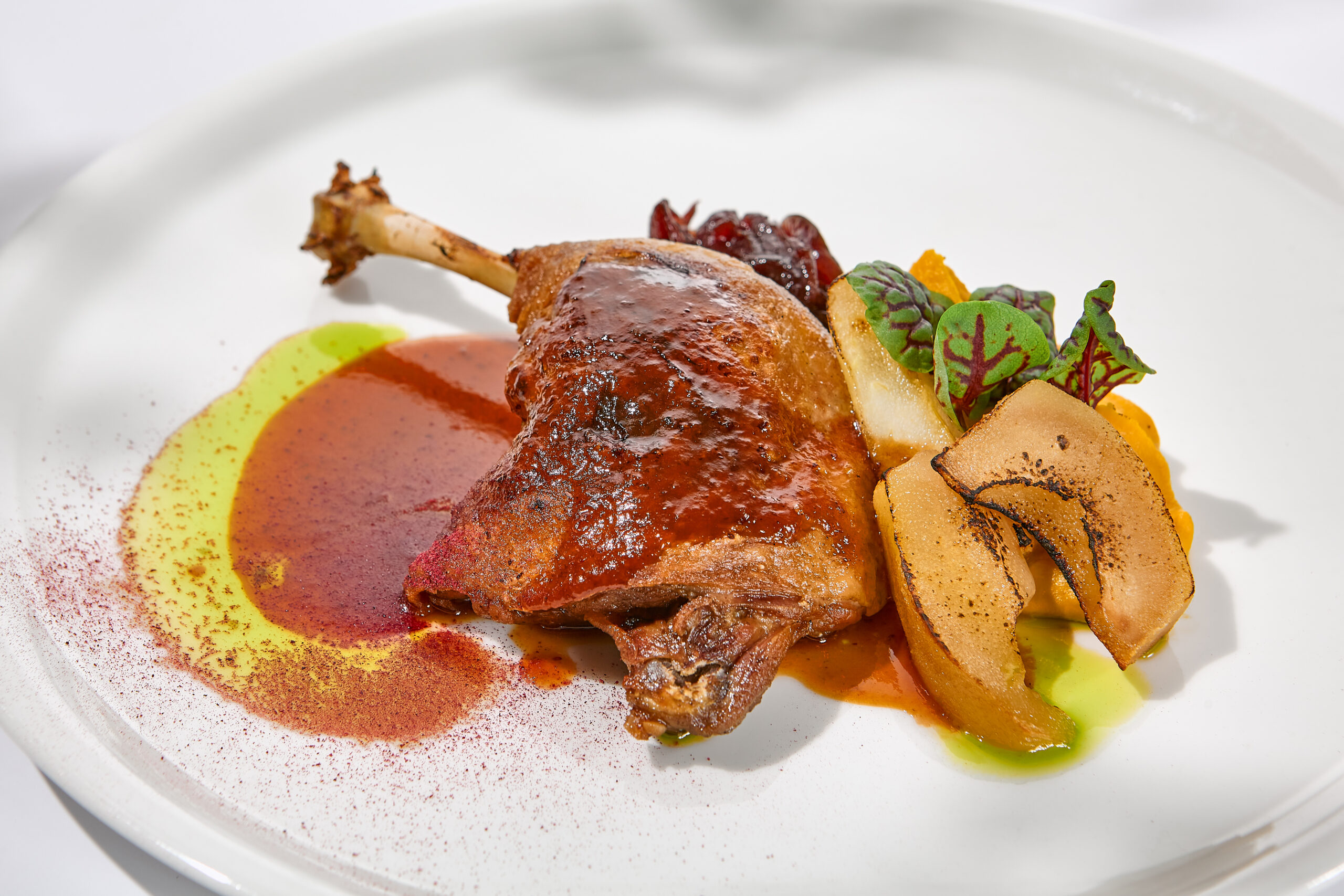 Traditional france dish - duck confit with baked apple on light background with shadows of sunlight. Roasted duck leg with fruits and gravy on white plate in summer dining. Elegant roasted leg