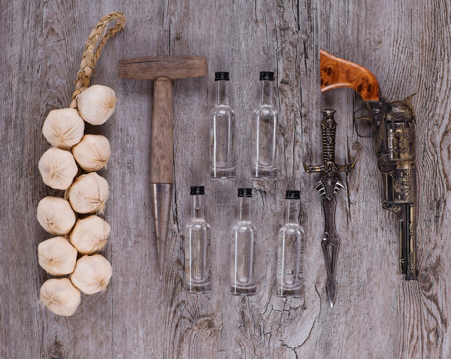 weapons against vampires: garlic garland, cross, holy water bottles, gun, on table