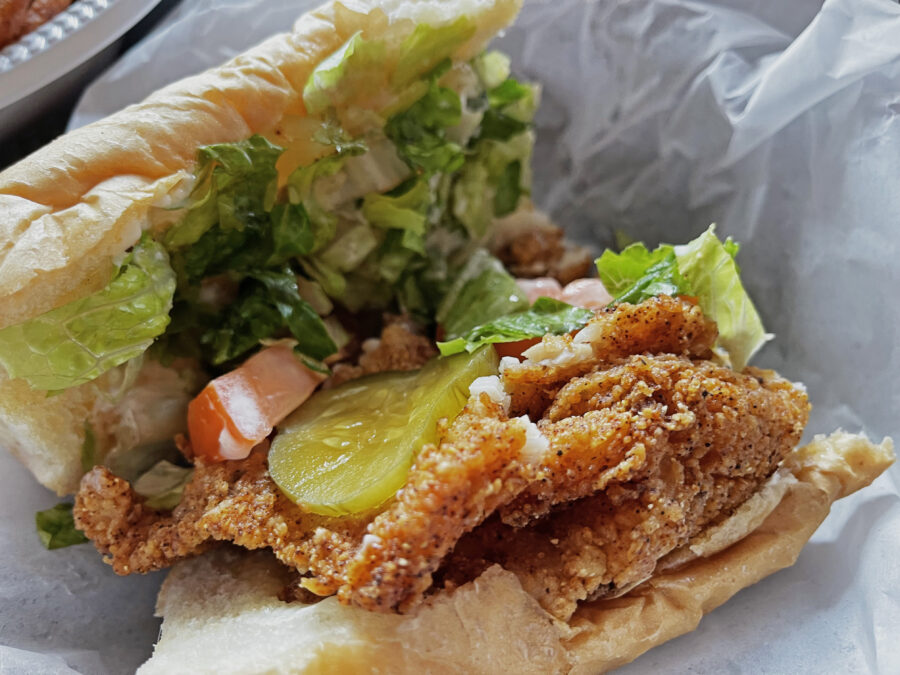 A fried catfish po'boy.   Half eaten.  Pickles, lettuce, and tomato.