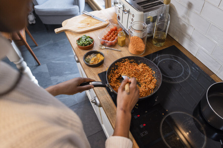 An over the shoulder shot of a young woman preparing a vegan meal in the kitchen. She is cooking a dhal curry in the pan.