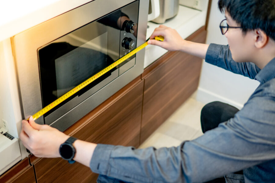 Asian man interior designer using tape measure on microwave oven in the kitchen showroom in furniture store. 