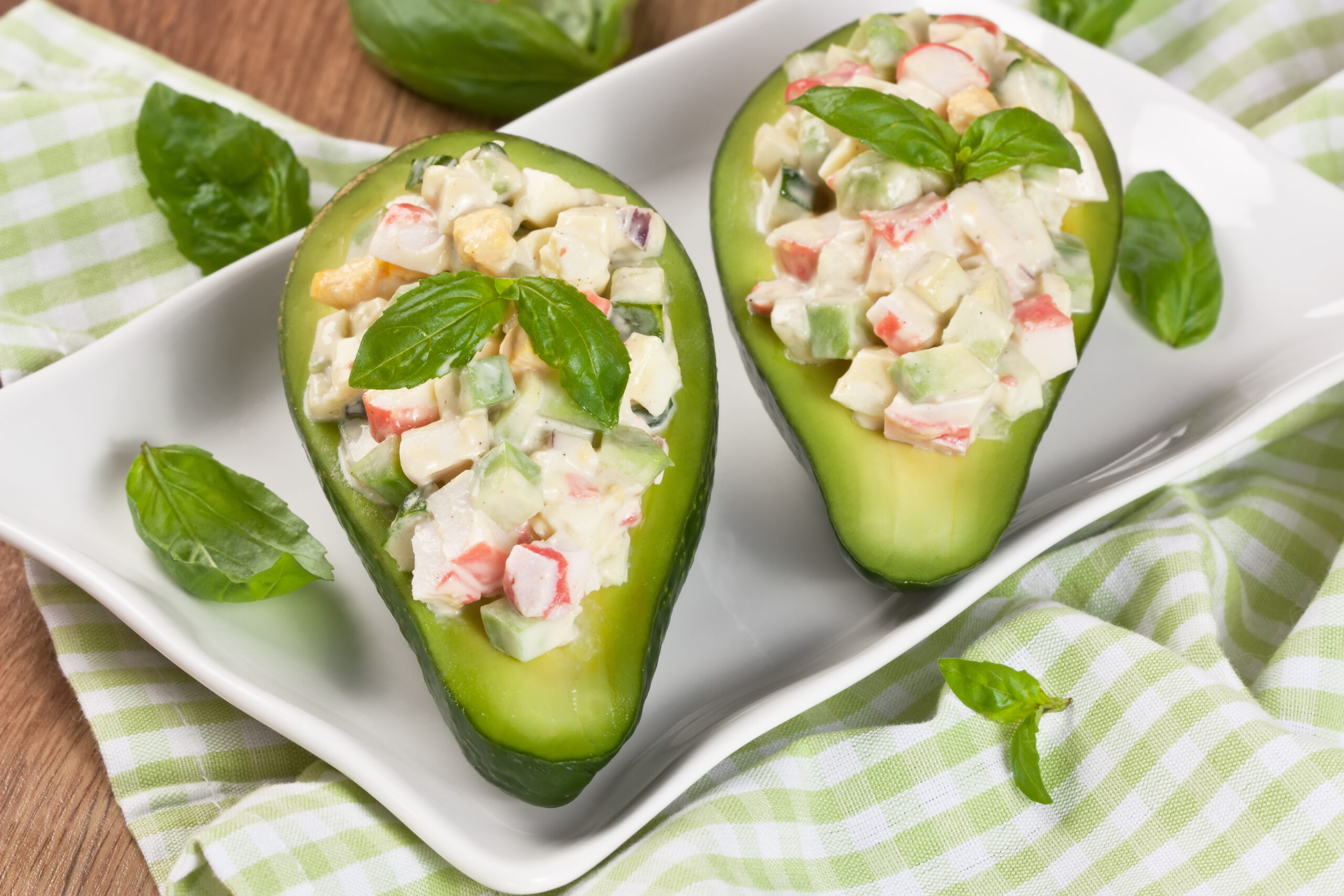 Avocado stuffed with crab, cucumber, egg, red onion and sauce mayonnaise on white plate