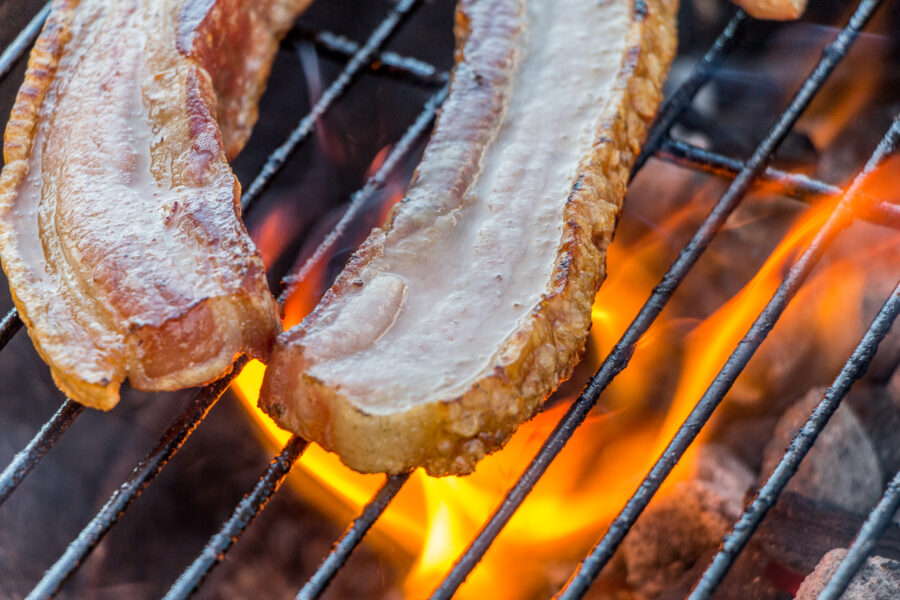 Bacon on barbecue grill. Fire at background