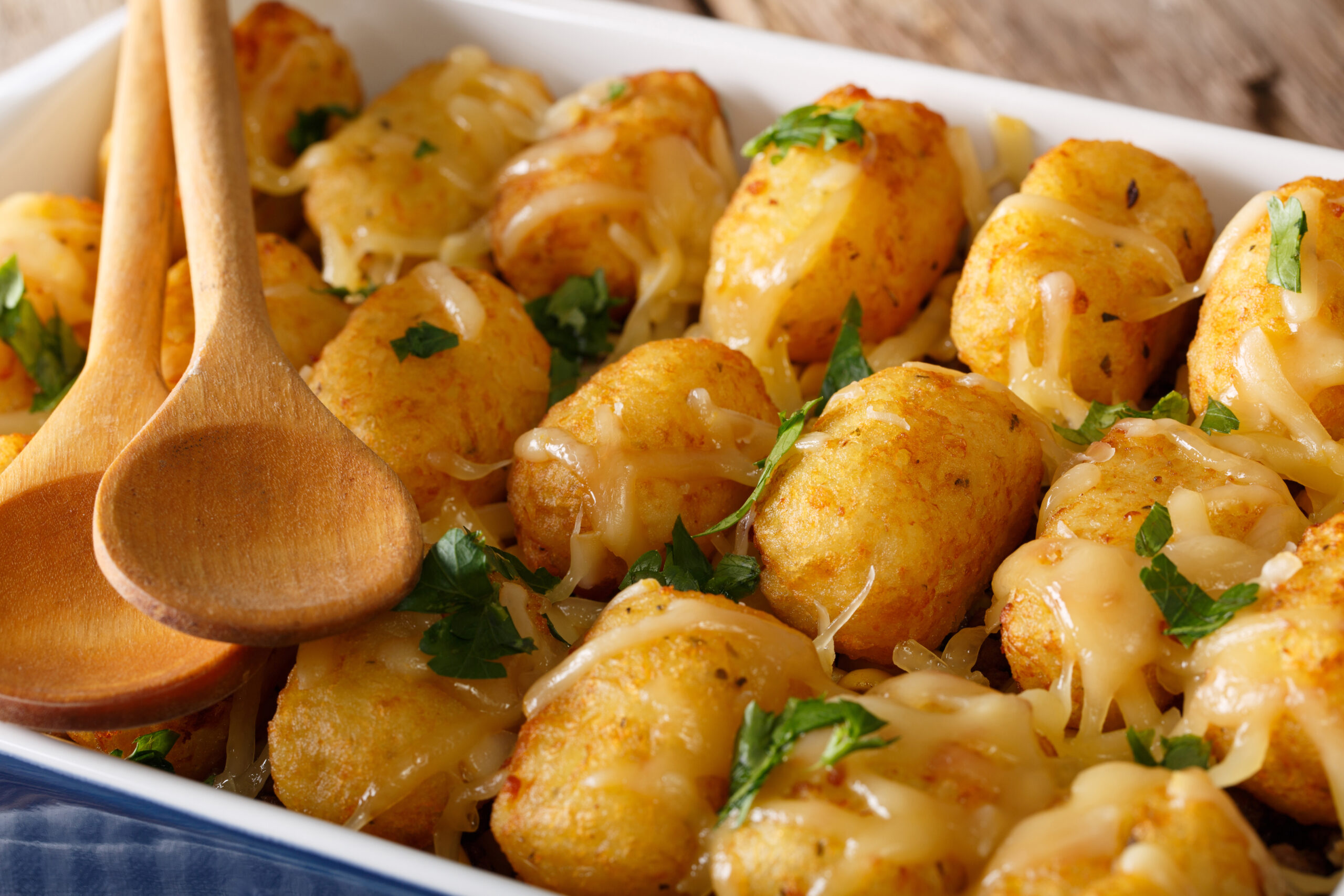 Baked Tater Tots with cheese and herbs close up in a dish baking dish on the table. horizontal