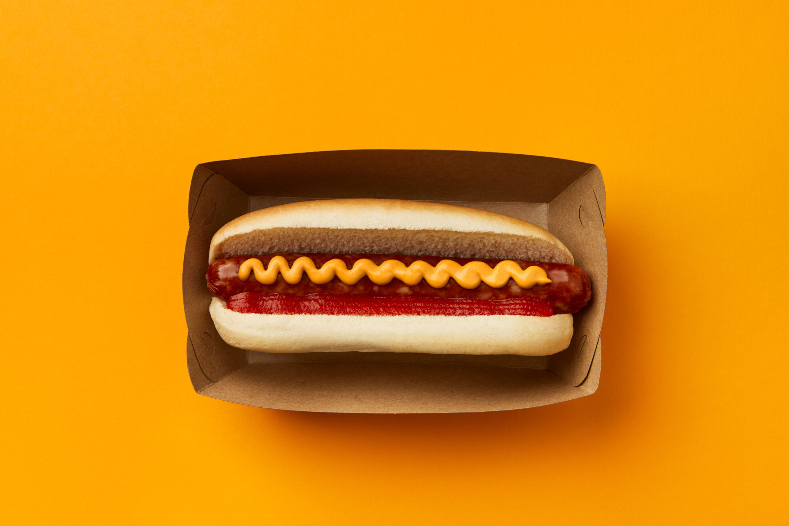 Classic hot dog with wurst, ketchup and mustard on orange background. Restaurant menu delivery tacke away concept. American cuisine street food