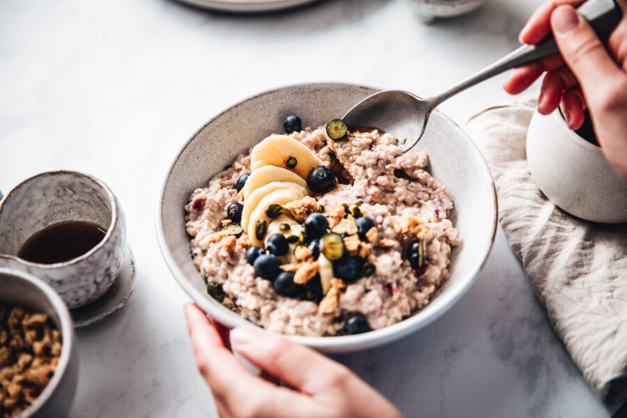 Close-up of a woman mixing oats flour, banana and blueberries in a bowl. 