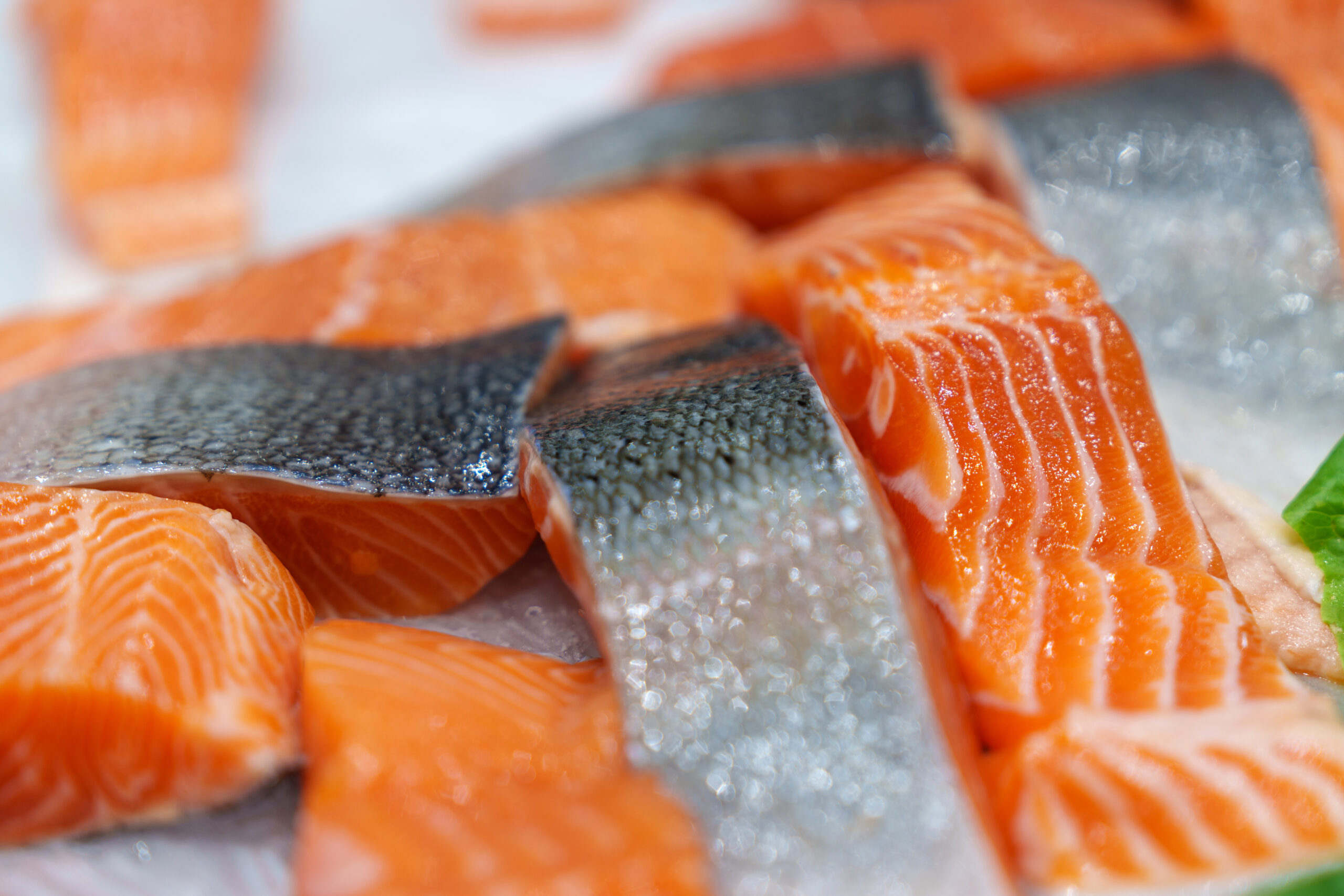 Close up view of fresh raw salmon fish fillets and steaks are displayed on crushed ice in a retail setting.