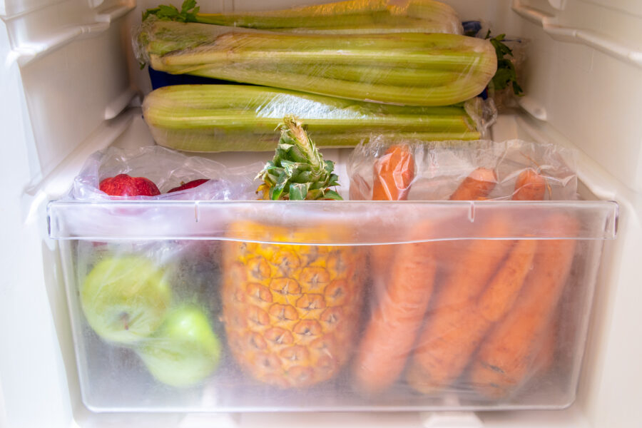 Colorful fruits and vegetables in fridge crisper - apples, pineapple, carrots, celery