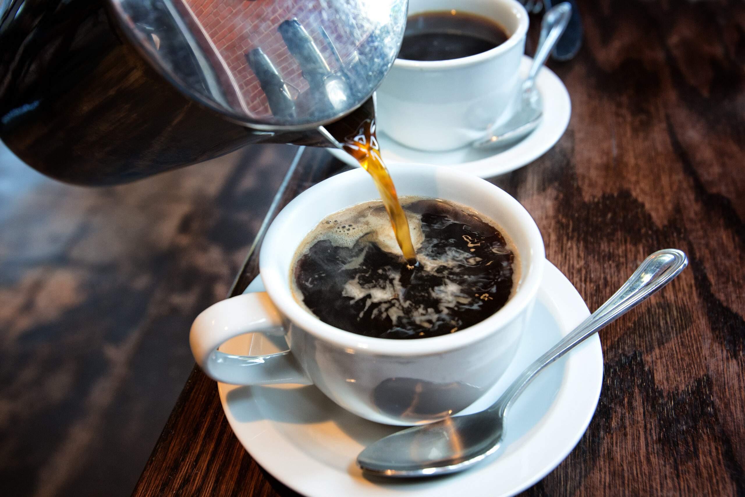 Fresh hot coffee being poured into a cup from a stainless steel french press in a trendy cafe