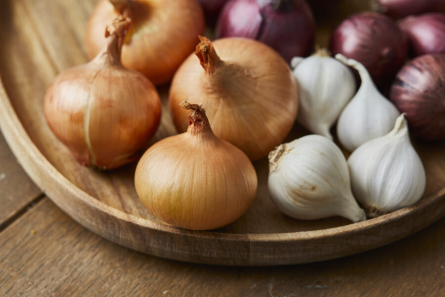 Garlic, onion and Spanish onion on a wooden plate, seasoning vegetables on a wooden kitchen table top, a top view 