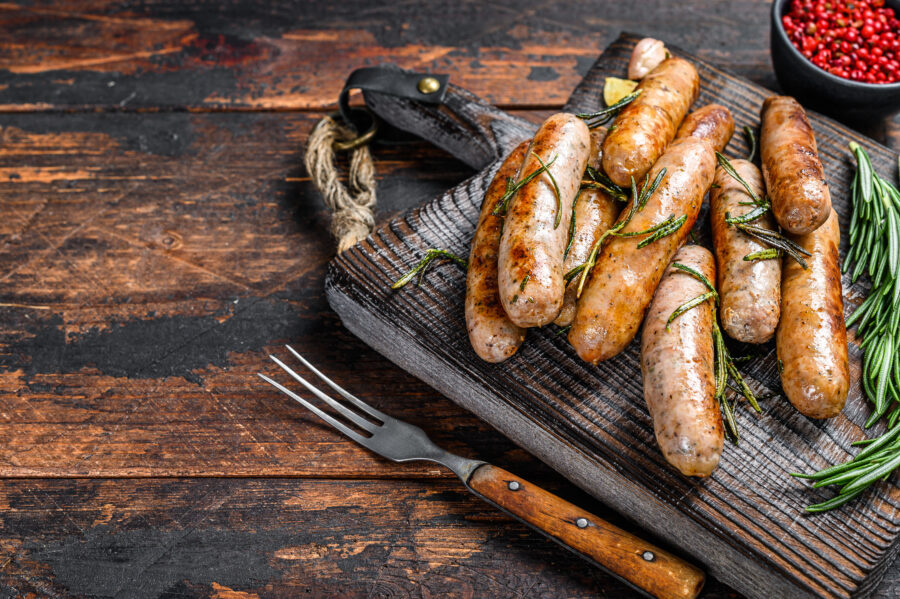 Grilling bavarian sausages on a cutting board. Dark wooden background. Top view.