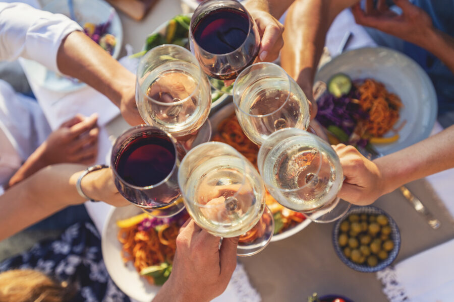 Group of friends having a meal outdoors. They are celebrating with a toast using wine. There are plates of food on the table including olives, salad and spaghetti Bolognese. Multi ethnic group.