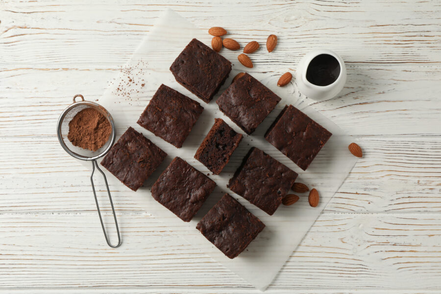 Chocolate cake slices, almond, strainer and chocolate on white background, top view