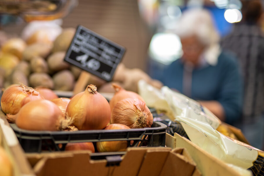 Close-up of onion at vegetable market, with blurred female customer buying food in background