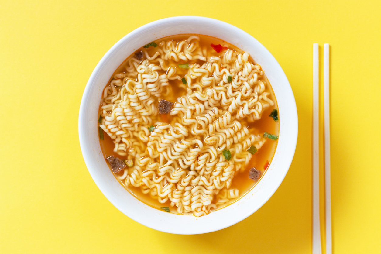 Instant noodle soup in a white bowl on a yellow background top view.