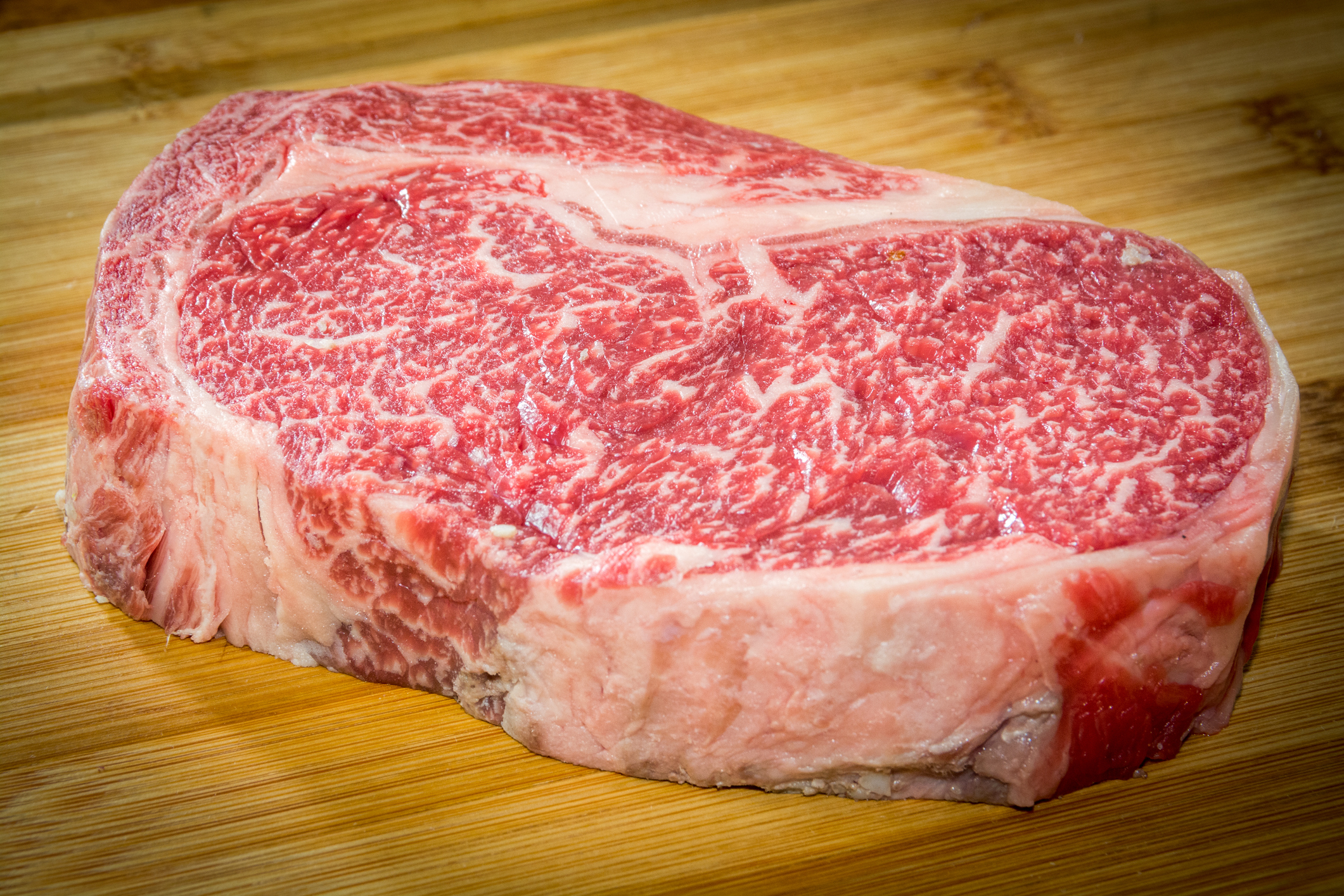 An amazingly well marbled steak is displayed on a wooden cutting board.  This thick cut 100% full blooded Wagyu rib eye is a stunner.