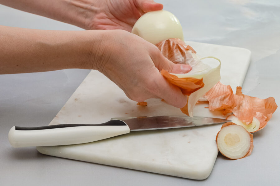 A woman hands peeling white onion with knife, close up view, marble kitchen table background