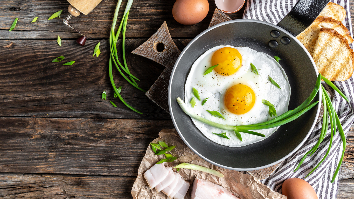 Ukrainian breakfast Scrambled eggs in frying pan with pork lard, bread and green feathers onions. Long banner format, top view.