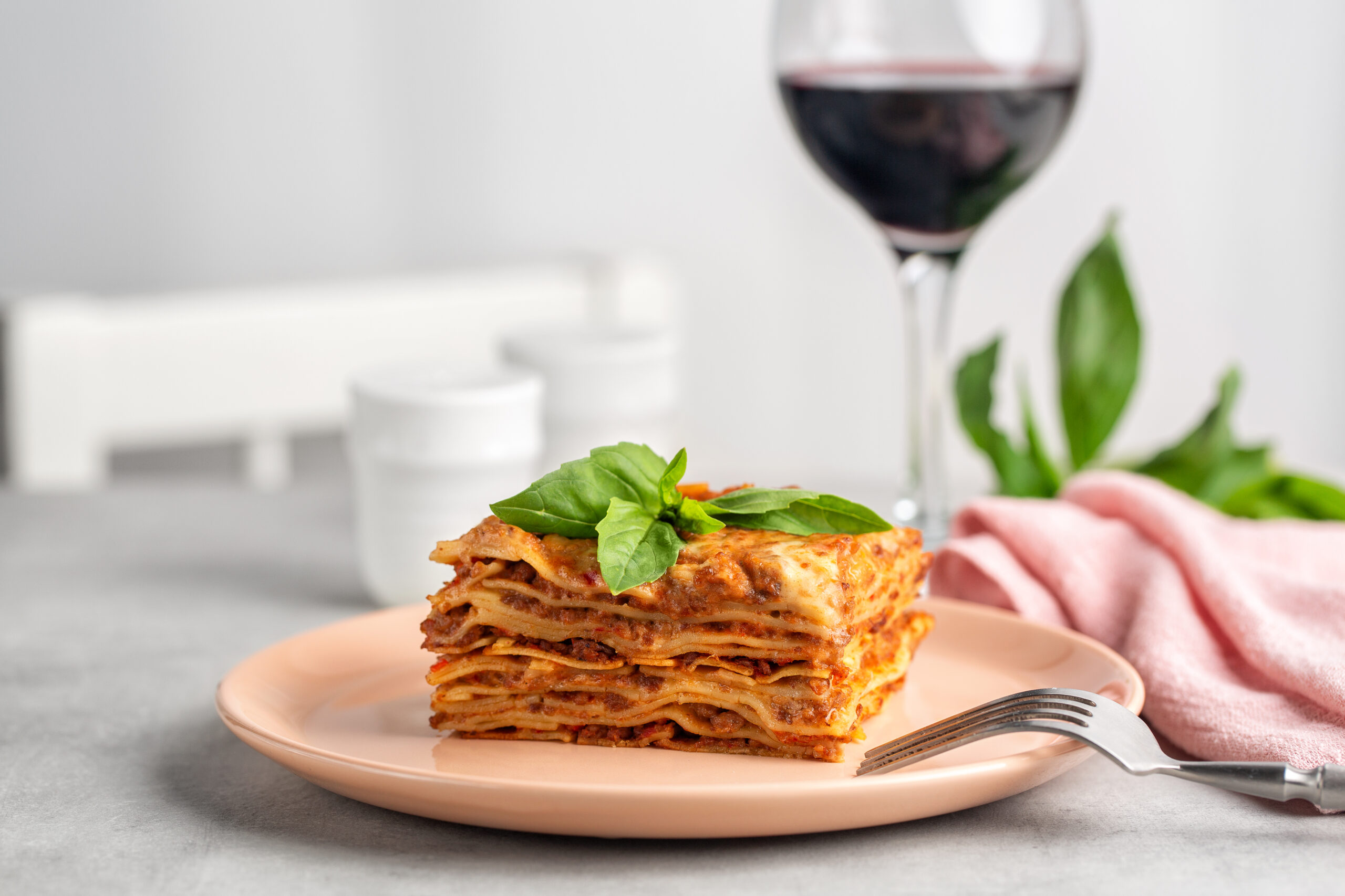 Italian dinner. Meat lasagna decorated with basil leaves and red wine glass. Light table.