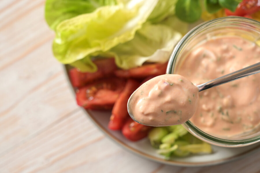 Thousand Island sauce based on skyr on a spoon and in a glass jar over slices of lettuce and tomato salad, healthy raw food meal, selected focus, very narrow depth of field