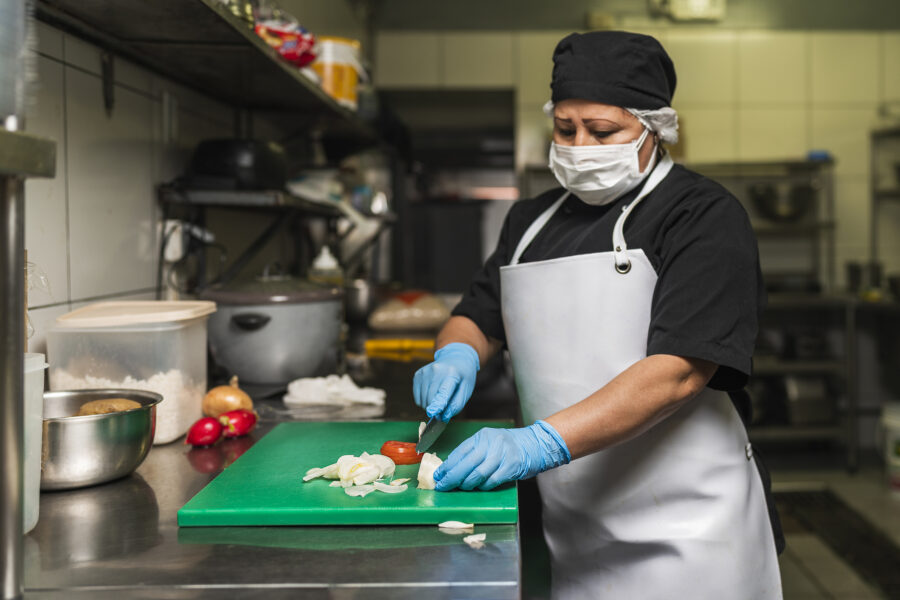 Professional cook in uniform cutting onions on a plastic board at kitchen of restaurant