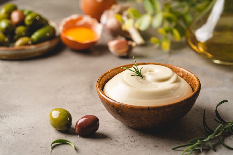 Bowl of mayonnaise with olives, ingredients and herbs