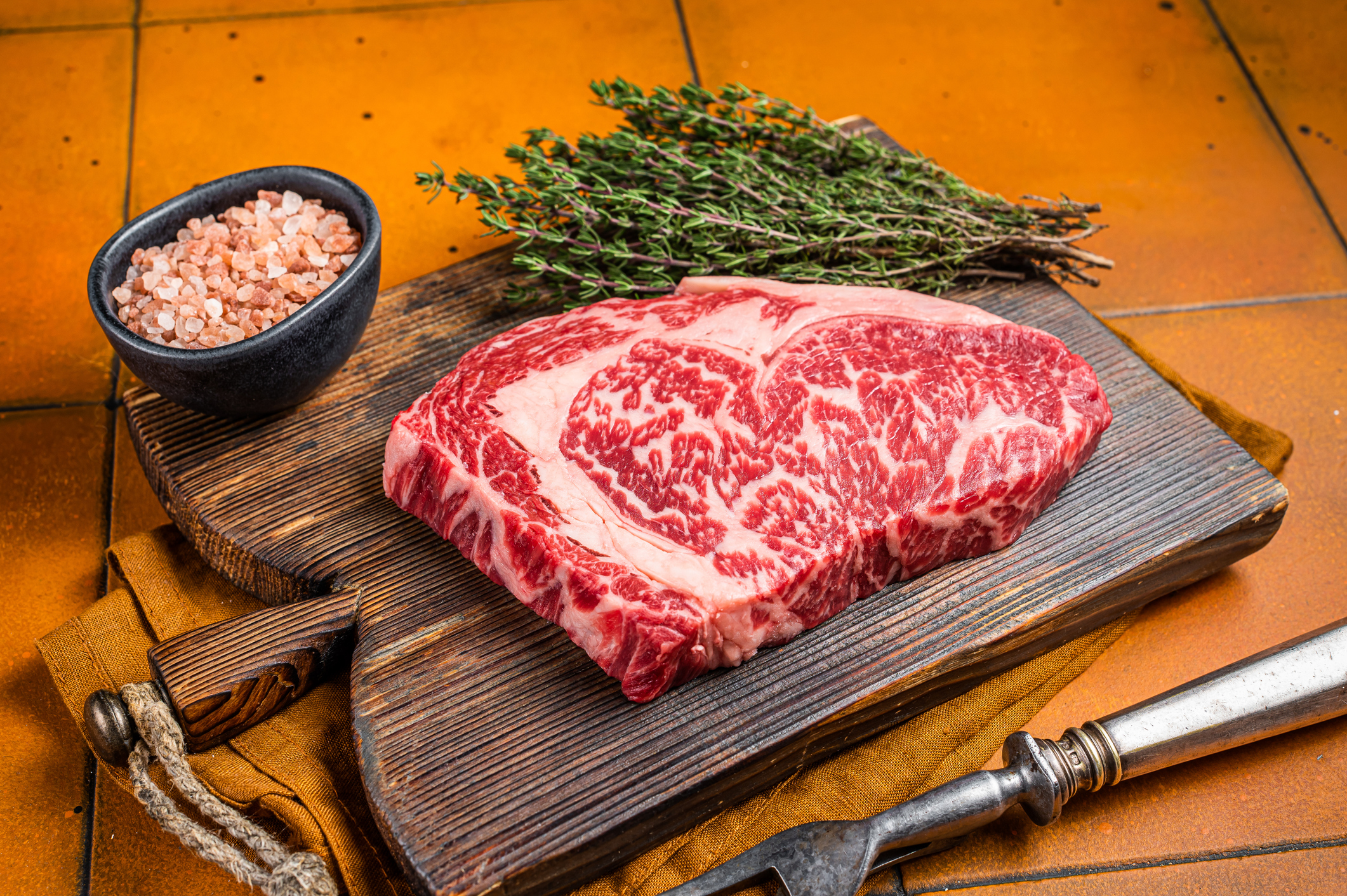 Prime Raw wagyu Rib Eye beef meat steak on wooden board. Orange background. Top view.