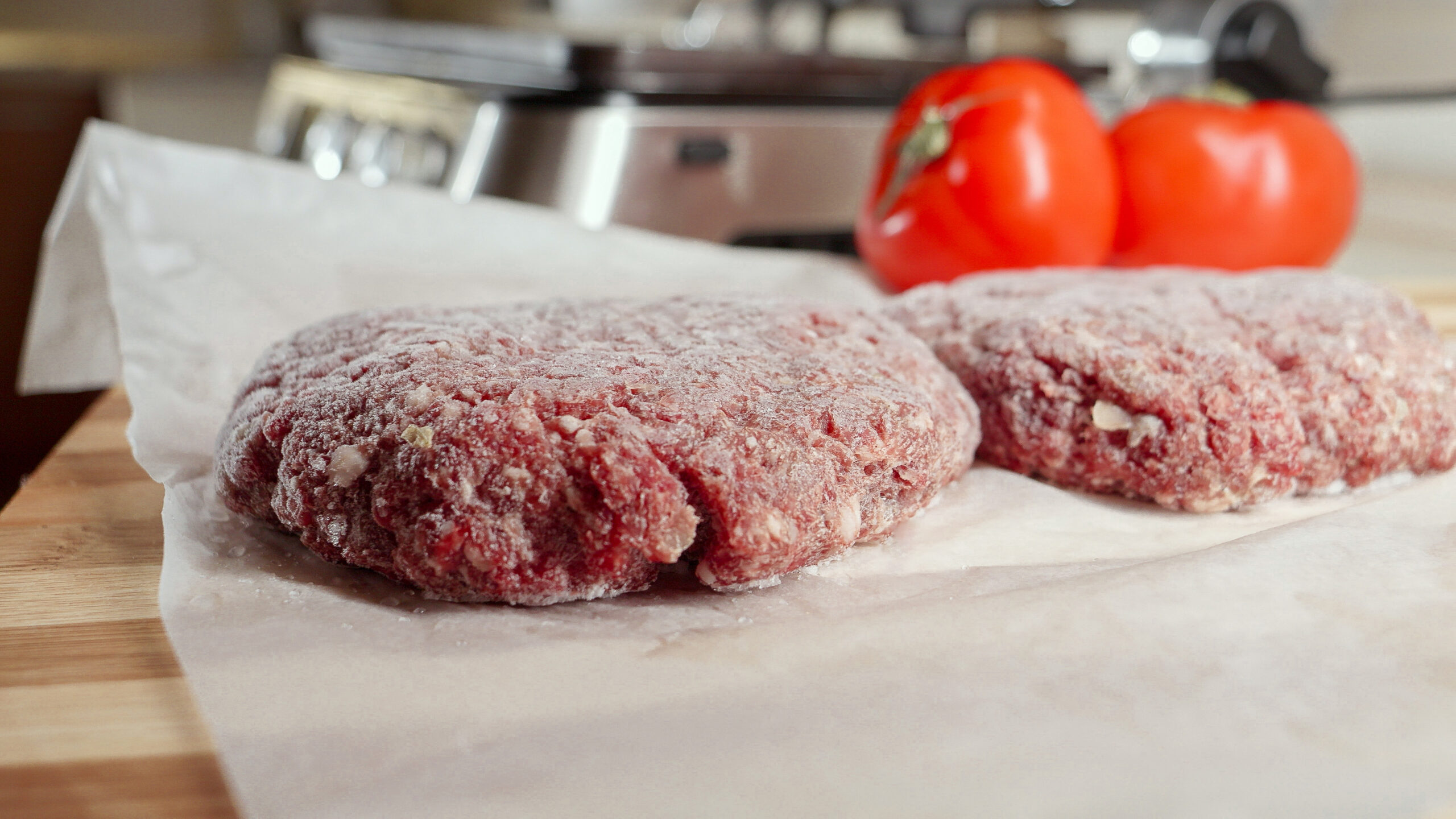 Frozen hamburger patties and ingredients lying on kitchen table next to electric grill