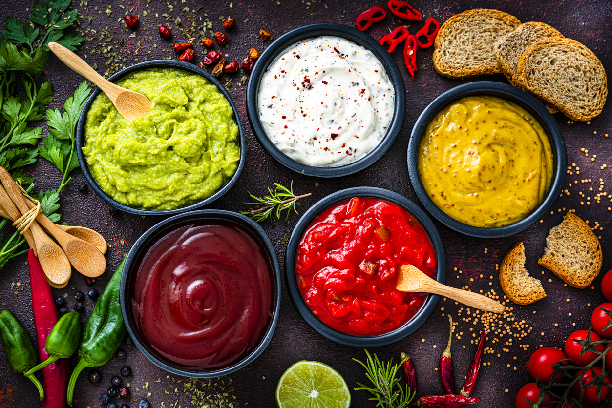 Set of five dip sauces shot from above on dark table. The composition includes guacamole, mayonnaise, Dijon mustard, hot sauce and barbeque sauce. High resolution 42Mp studio digital capture taken with Sony A7rII and Sony FE 90mm f2.8 macro G OSS lens