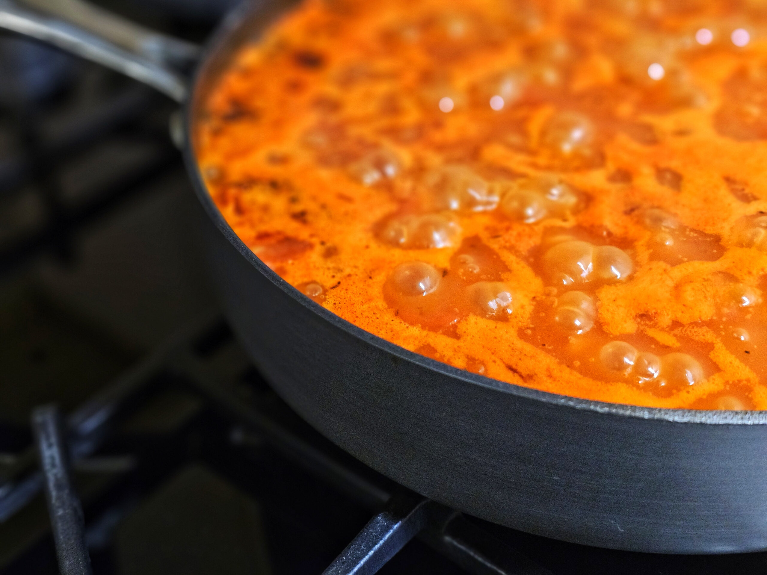 A pan of paella cooking and simmering on the gas hob.