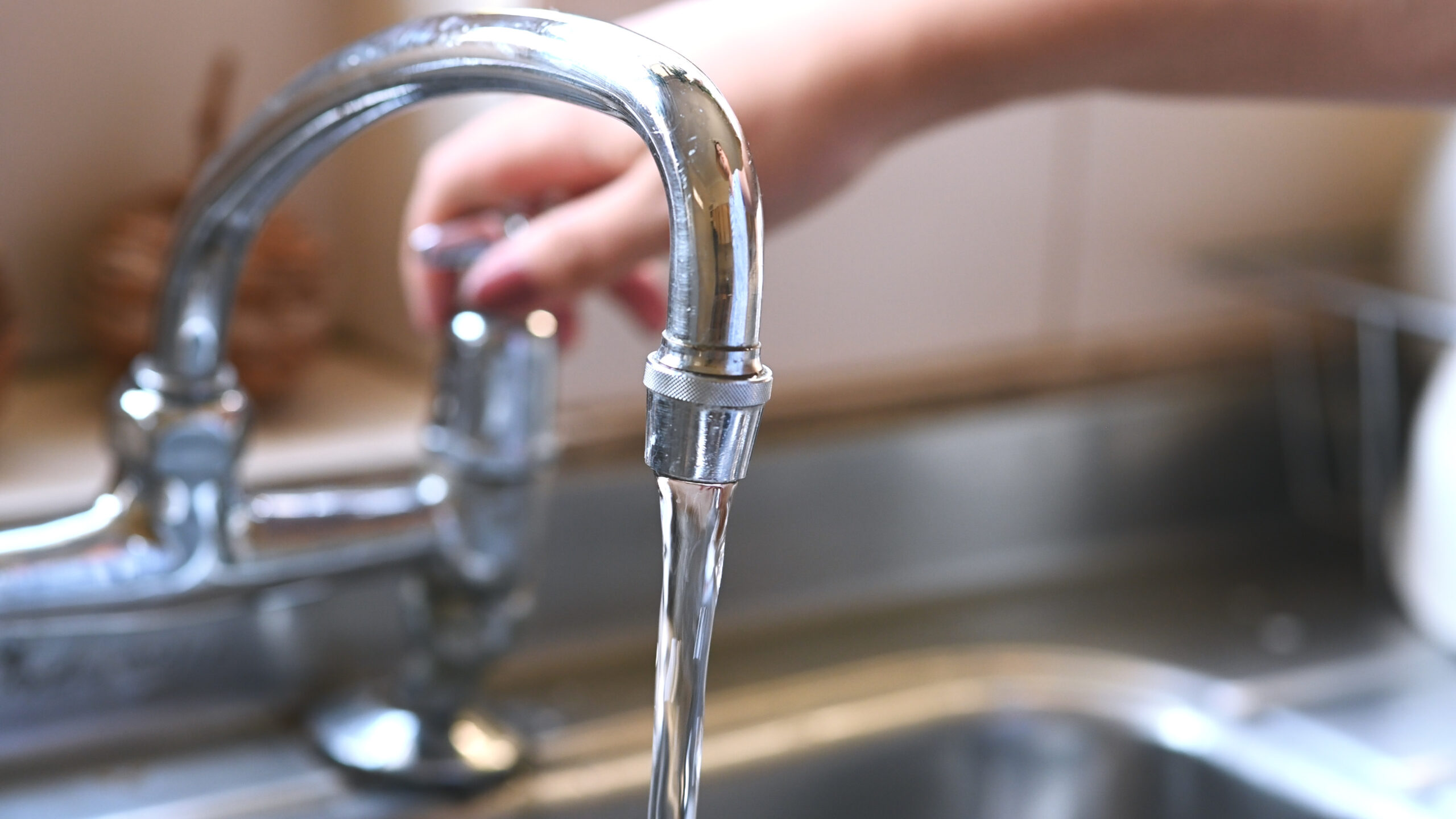 Open, water and faucet with hand of woman in kitchen for cleaning, drinking and washing dishes. Interior, steel and household plumbing with sink and tap at home for stream, flowing and splash