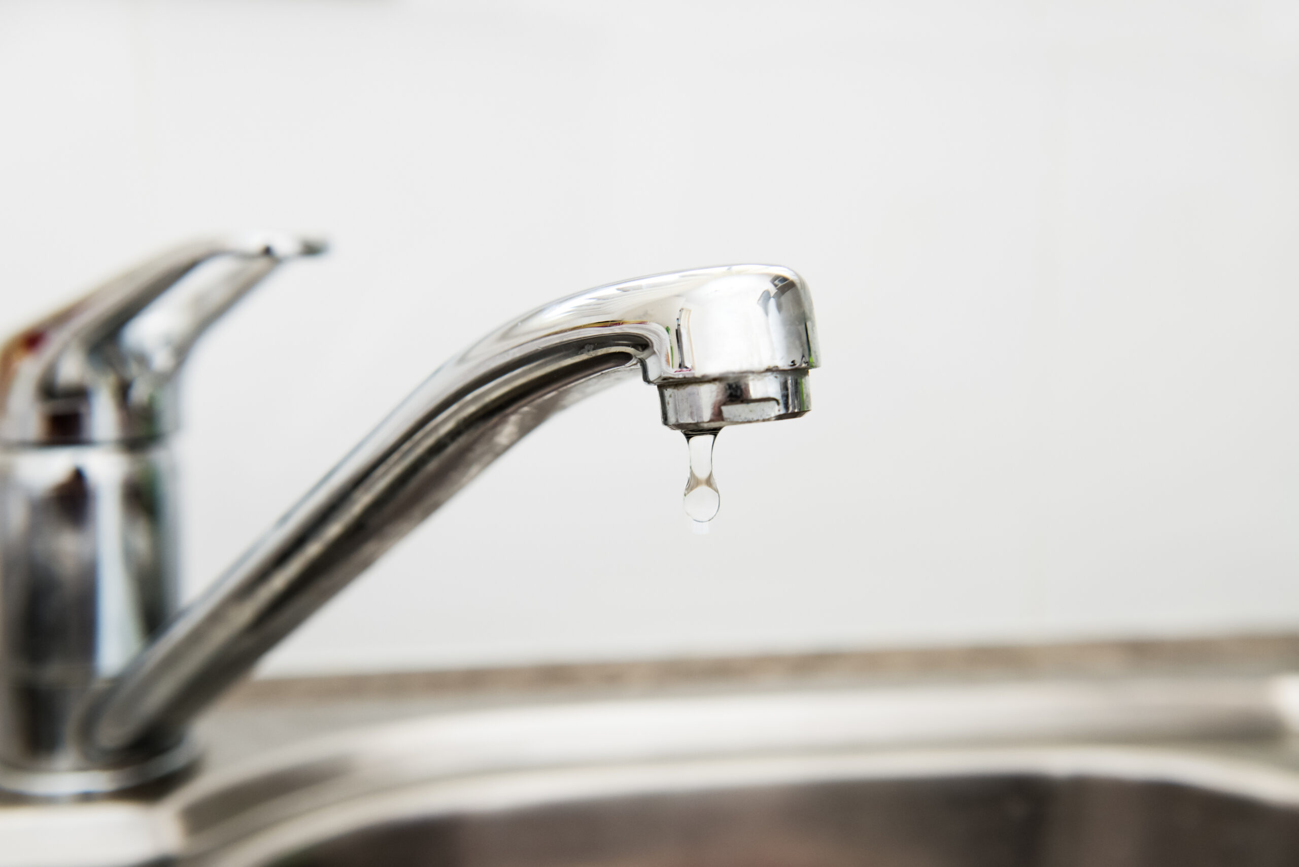 Modern stainless steel faucet and sink in the kitchen, on top of sink leaking and dripping water, selective focus of a leaking tap, could use a plumber to fix it