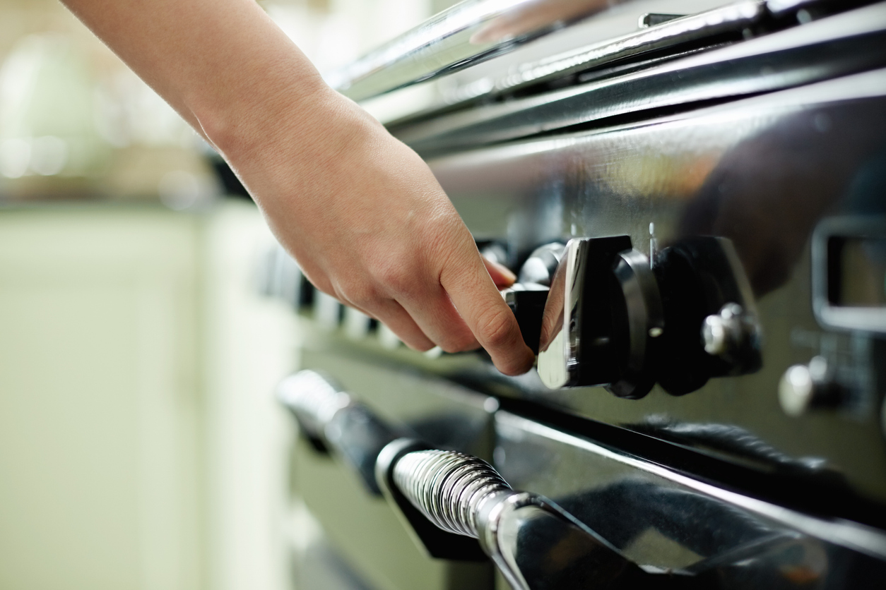 Cropped image of female hand turning stove controller. Woman is operating black oven knob. Appliance is in kitchen at home.