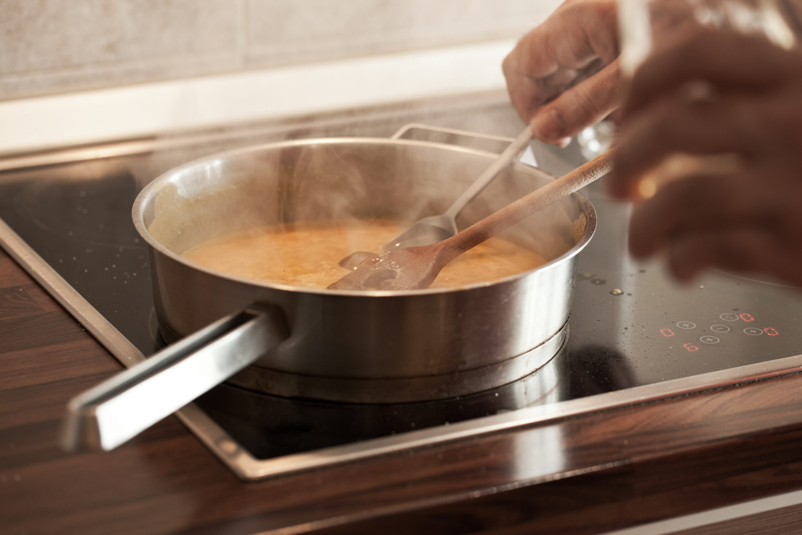 Honey mustard sweet sour sauce cooking in hot pan at stove; close up; Chef's hand taking sample into spoon;