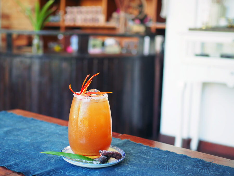 Salted rim of beautiful mocktail glass of iced tamarind juice decorated with carved chili served with dried tamarind, selective focus.