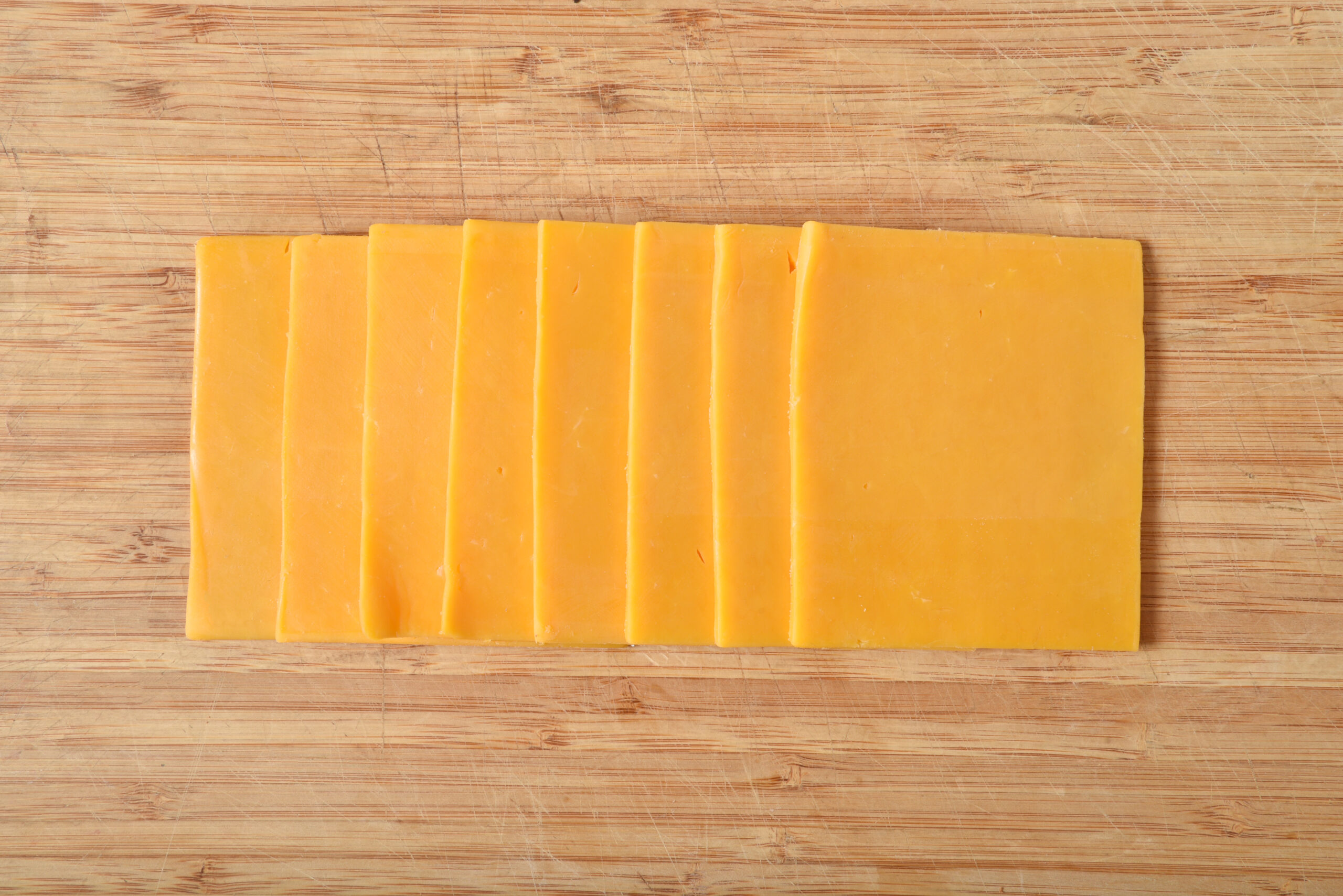 Overhead view of cheddar cheese slices on a cutting board